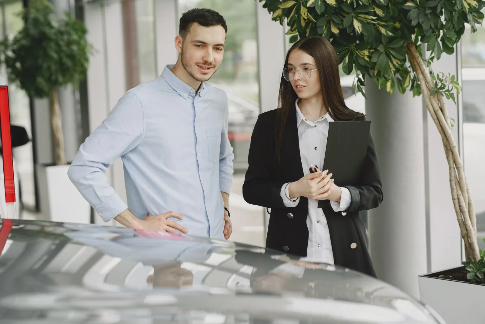 Customer and sales adviser standing beside a vehicle in a car dealership showroom